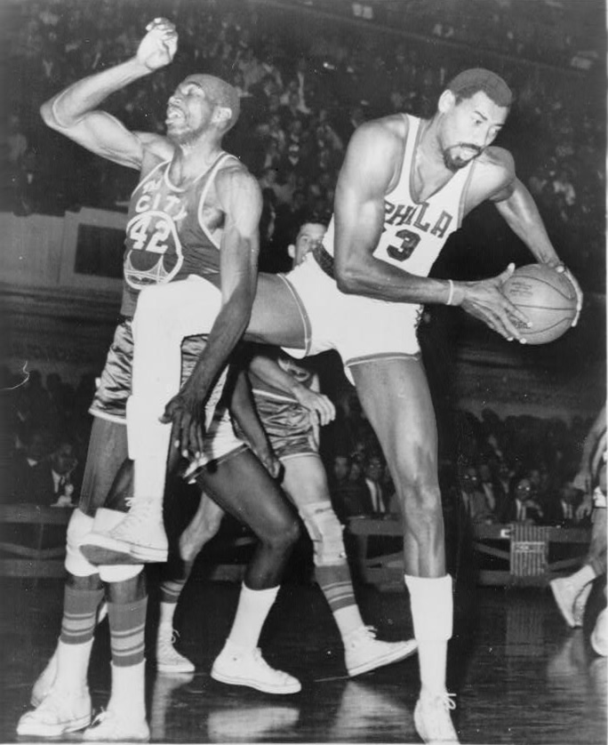 Coming down with a rebound, Wilt Chamberlain plays in a game for the Philadelphia 76ers. Chamberlain is the leader in rebounds per game over a career and rebounds in a single game. 
