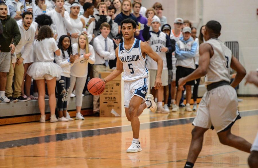 Dribbling+down+the+court%2C+returning+Varsity+player+and+senior+Phillip+Burwell+has+his+eye+on+the+competitor.+Behind+him%2C+the+Maniac+section+is+cheering+in+support%2C+giving+the+team+plenty+of+energy+to+feed+off+of.+%0A