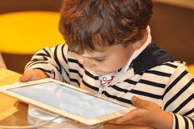 Staring at a tablet, a young boy amuses himself by playing with a mobile device. Children at such a young age can potentially be harmed physically, mentally, socially, and cognitively by too much screen time.