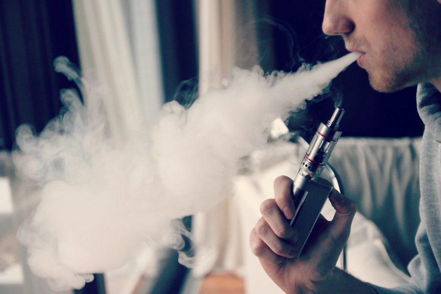 Exhaling a cloud of water vapor, a man demonstrates using an e-cigarette for recreation. Although the use of vapes is marketed as a way to quit smoking, the flavors of nicotine juice have drawn the attention of young people, some of whom are now experiencing health issues from the chemicals in said juice. 