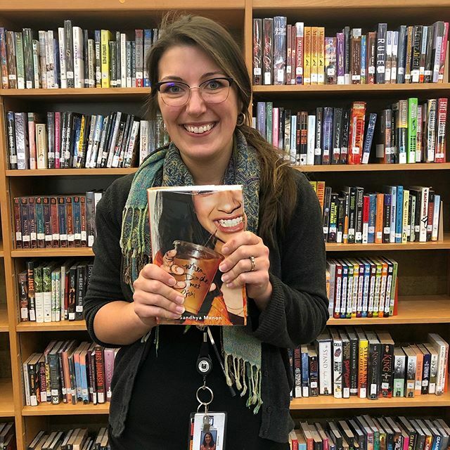 Smiling proudly, librarian Ms. Genesky poses with one of her new favorite romance novels. Finding a genre that you like will encourage you to read more and be able to reap the benefits that books offer. 
