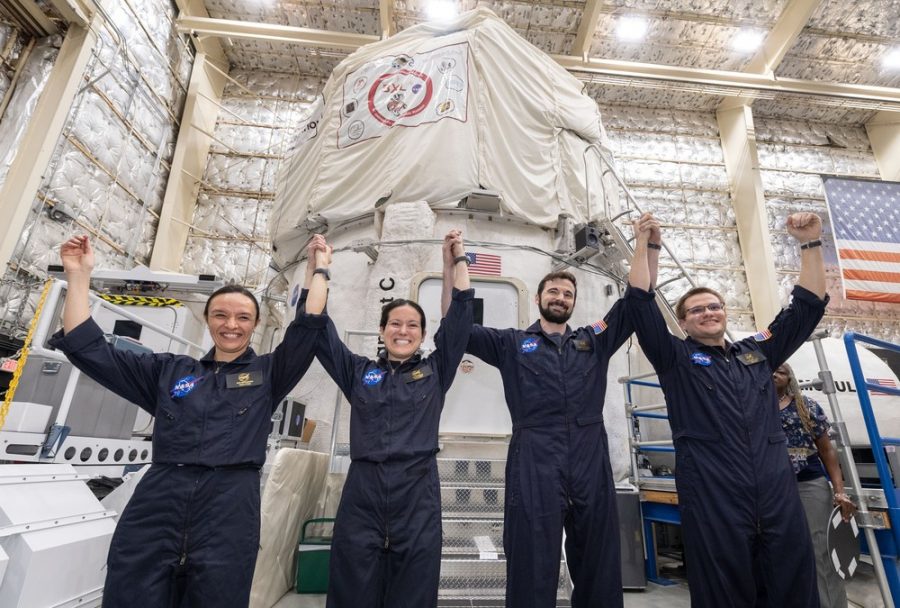 Holding their hands in the air, the four members of the Mars Mission smile proudly. The chosen ones stand ready to take the picture in commemoration of their first group meeting since they volunteered.