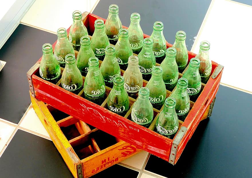 Nestled in wooden crates are vintage glass Coke bottles. Glass soda bottles like these, made from renewable material, are one way that we can learn from the past about being more eco-friendly and to assess changes we can make today.