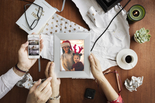 Unwrapping a gift, the recipient holds a sentimental framed photo. While most photos are digital, printing photos or making a scrapbook for family and friends can make a thoughtful and useful gift.