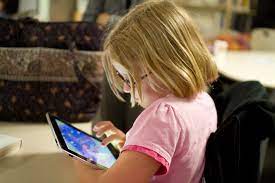 A young girl sitting down, playing games on an iPad, is paying no attention to her other surroundings. Constantly playing on their phones can cause children to not grow appropriately in every aspect of their lives.