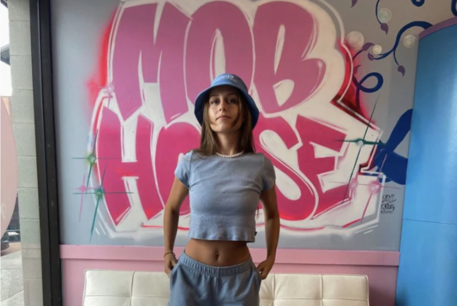TikTok influencer Georgia Costello stands in front of a graffiti wall promoting her brand. The growing social media creator has reached farther than simply making bikinis and now makes swim trunks for men as well as sweat suits for any gender.