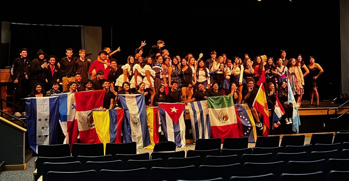 Members+of+the+Hispanic+Heritage+Show+take+a+group+photo+with+teacher+coordinator%2C+Mrs.+Amaguayo%2C+along+with+the+different+flags+of+Hispanic+countries.+